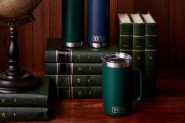 neatly stacked and organized dark green books against a dark dark wood background on a wood table with 3 YETI tumblers featured