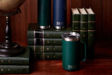 neatly stacked and organized dark green books against a dark dark wood background on a wood table with 3 YETI tumblers featured