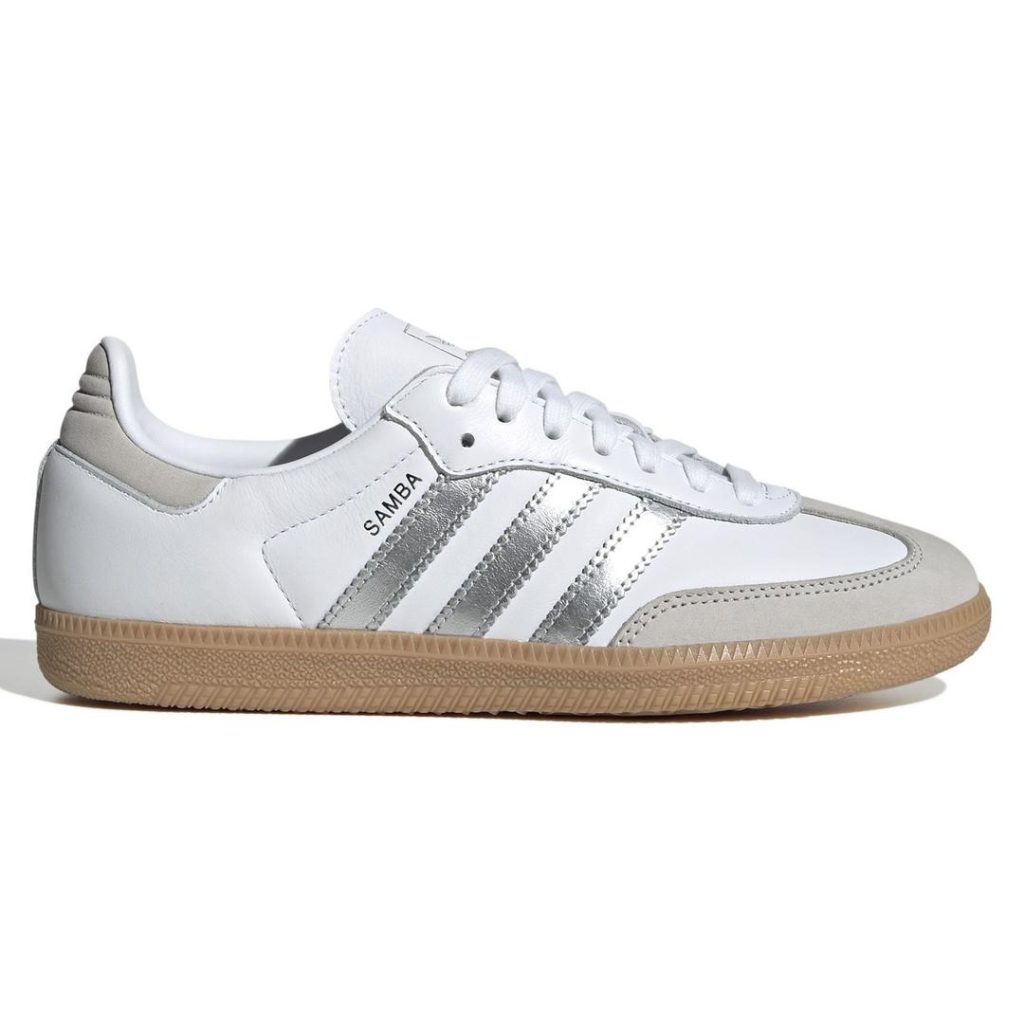 Smooth white leather low-top adidas sneaker with contrast grey detail at the back heel panel and around the front toes. Contrast metallic silver serrated 3-Stripes at the side with small "SAMBA" lettering. White laces on top. Contrast brown gum rubber outsole with light textured finish.