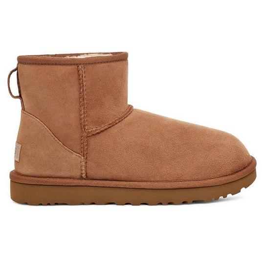 All brown suede short UGG boot with a heel pull loop and a brown foam sole. Off-white shearling lining peaking out from the top. follows back to school fashion trends